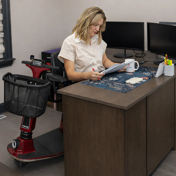 A woman sitting beside a table  on the swiveled chair of the Amigo RT scooter in red