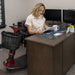 A woman sitting beside a table  on the swiveled chair of the Amigo RT scooter in red