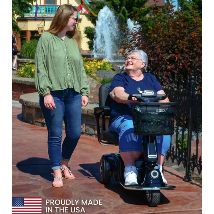 Woman in a wheelchair being assisted by another woman outdoors with a fountain in the background. Amigo HD Express 3 Wheel Mobility Scooter
