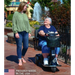 Woman in a wheelchair being assisted by another woman outdoors with a fountain in the background. Amigo HD Express 3 Wheel Mobility Scooter