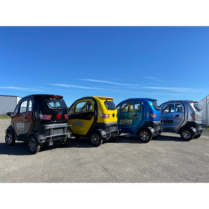 Four small GIO Enclosed All Season Mobility Scooter  electric cars in black, yellow, blue, and gray parked on a clear day.