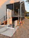 An outdoor residential wheelchai lift stairlift with an open ramp and open side door, installed at the entrance of a two-story house with a covered porch.