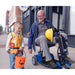 a man riding the Amigo travelMate scooter on a sidewalk with a child 