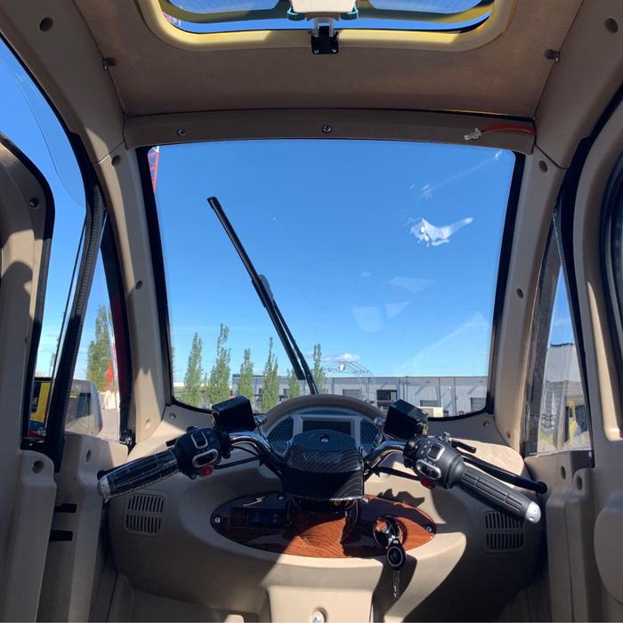 Interior front view of the GIO Enclosed Mobility Scooter showing handlebars, dashboard controls, windshield wiper, panoramic windshield, and roof skylight.