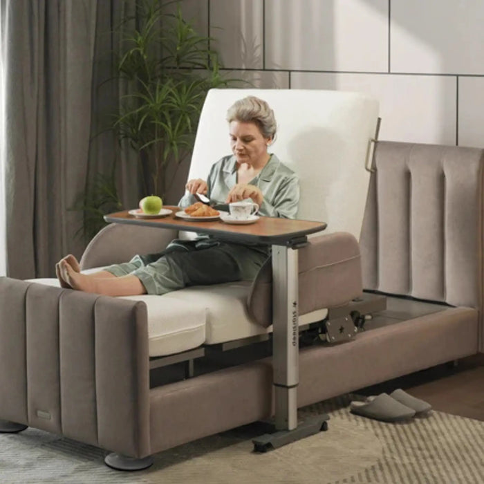 Woman seated comfortably in an adjustable bed using the StarSleep Motion Bed-Side Table for dining, with food and beverages placed securely on the tabletop for convenient bedside meals.
